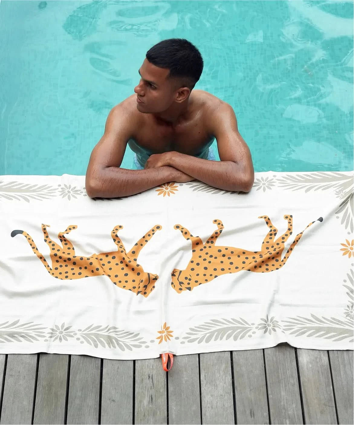 Person lounging by a pool with a towel featuring cheetah designs.